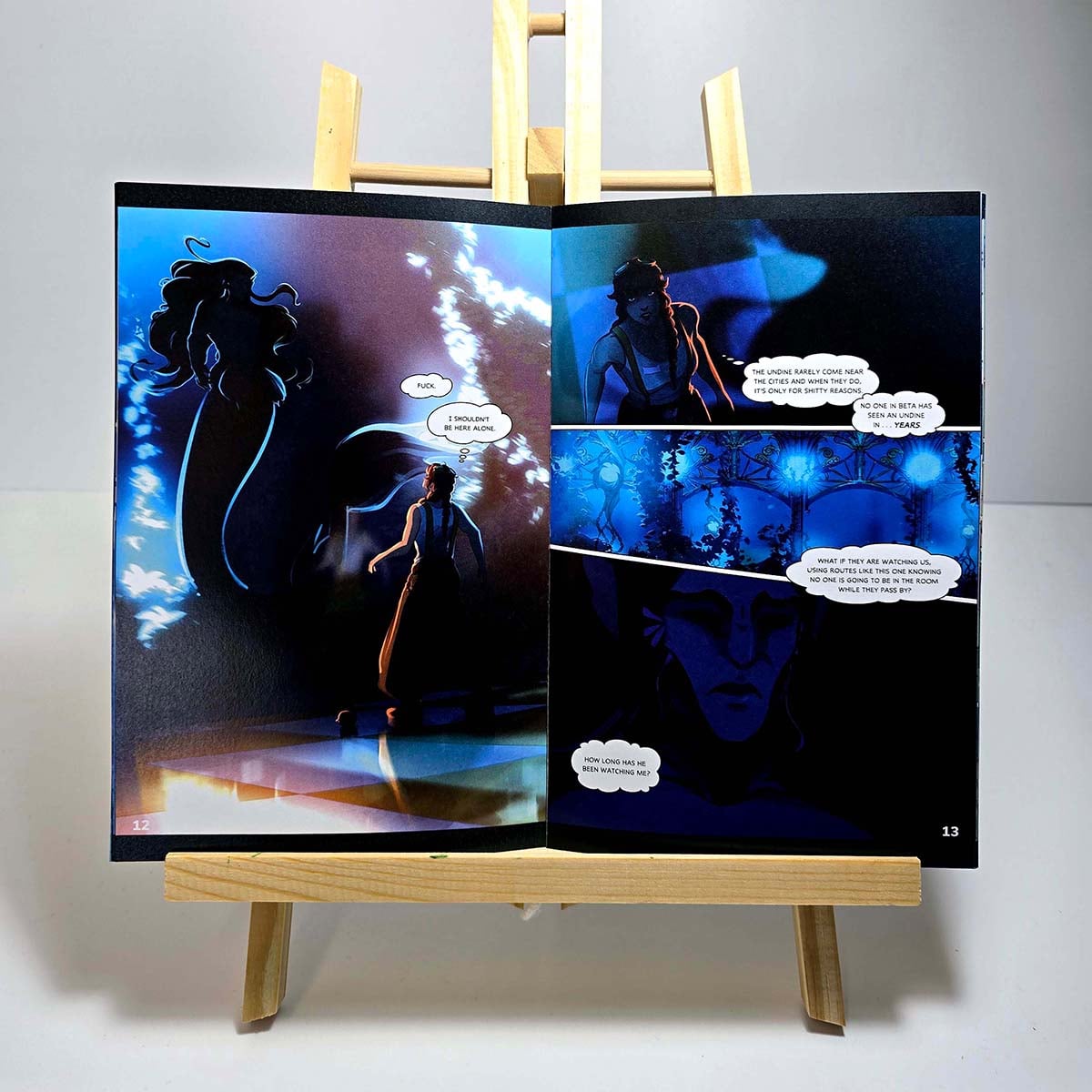 Listening Stars 28-page gloss comic book opened on an easel, showing dark blue illustrated interior pages with speech bubbles, comic panels, and glossy print finish.