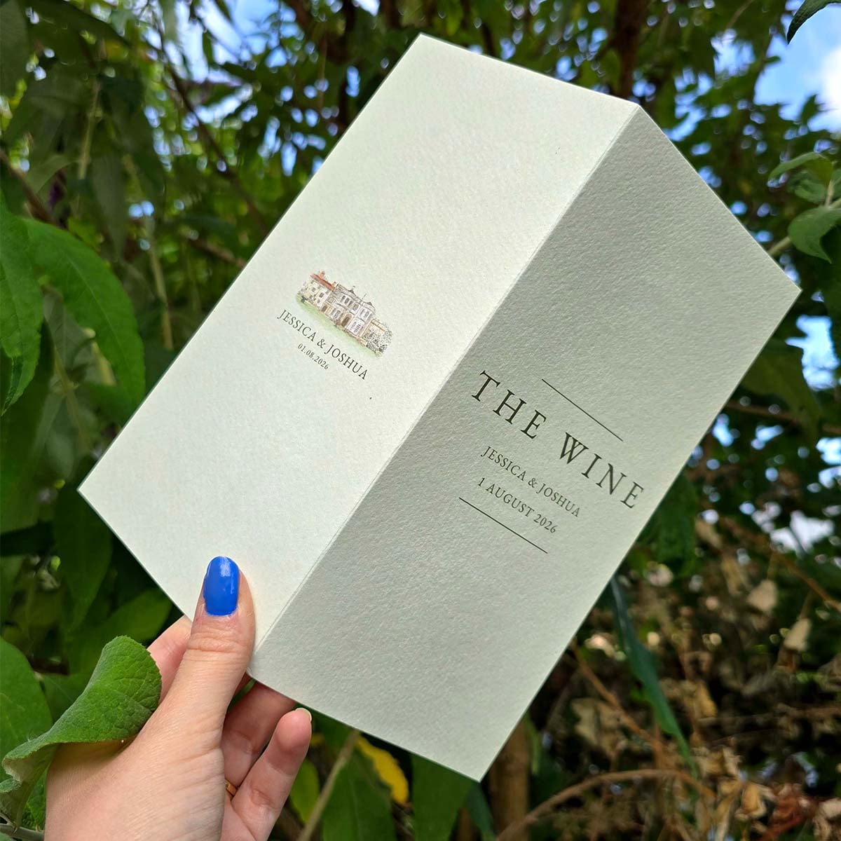 Open Fedrigoni Tintoretto Gesso wedding wine menu with textured paper, minimalist typography, venue illustration, and soft green wedding stationery design.